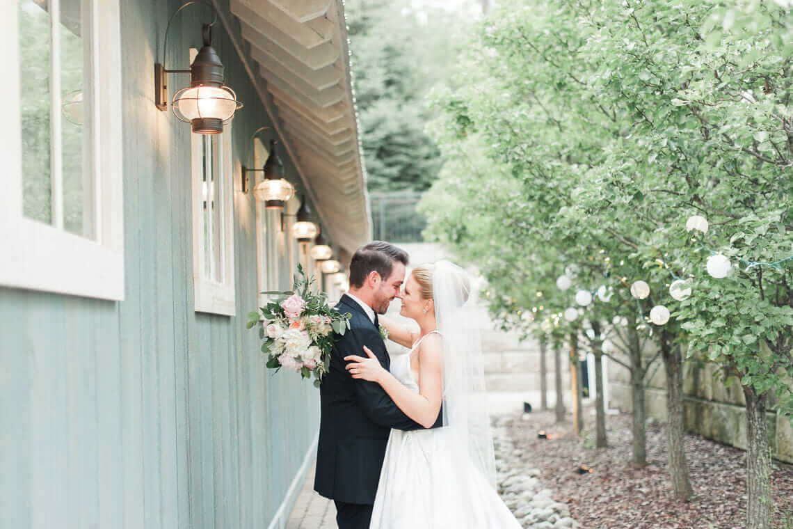 A bride and groom kiss in front of a blue barn during their wedding experience.