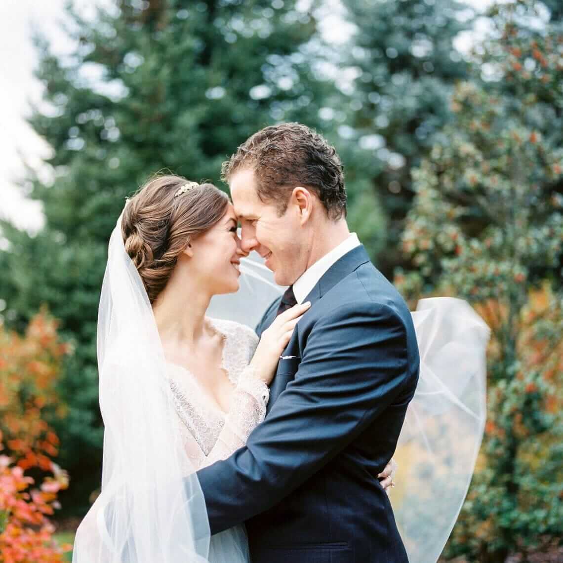 A bride and groom embrace in front of an autumn tree.