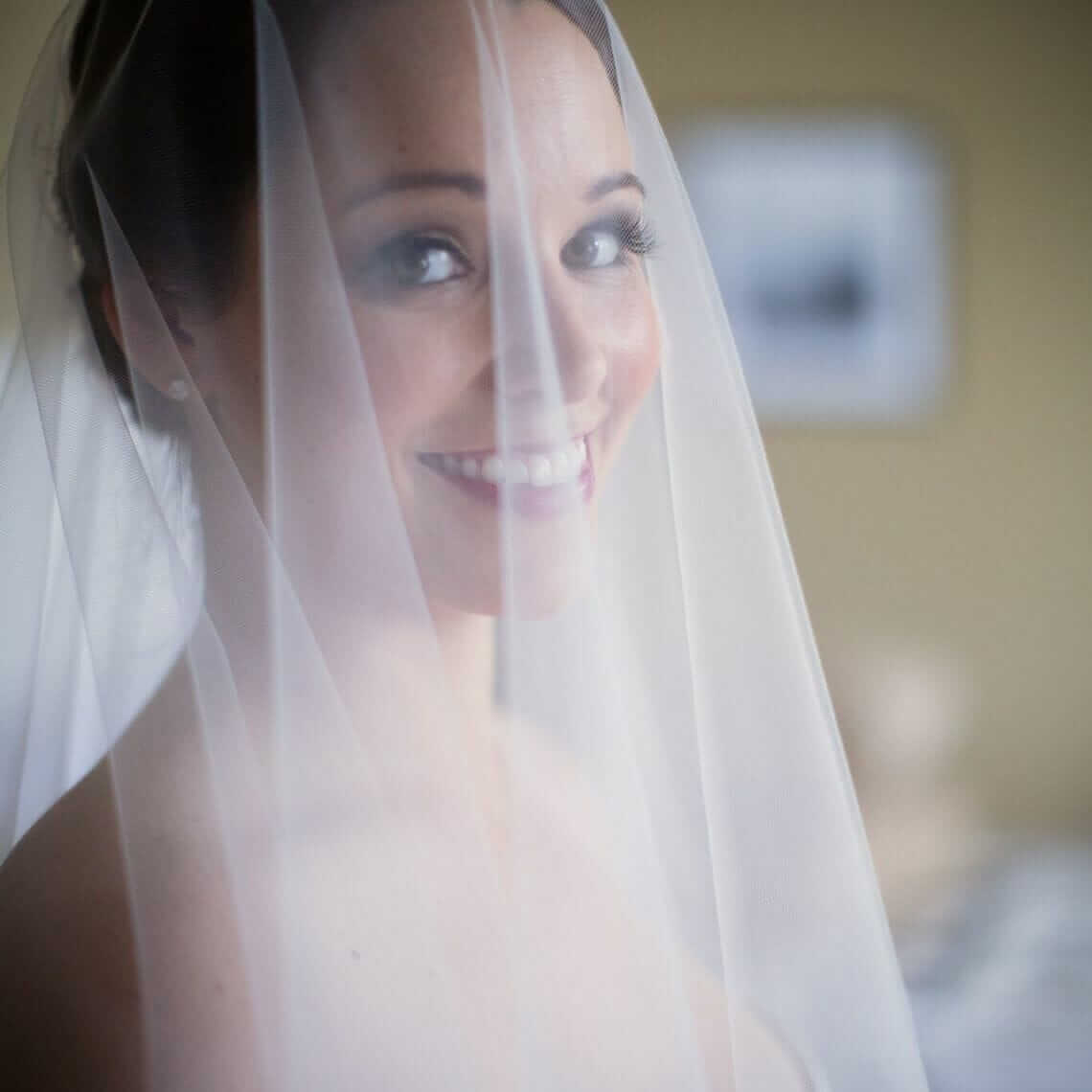 A bride wearing a veil in front of a bed.