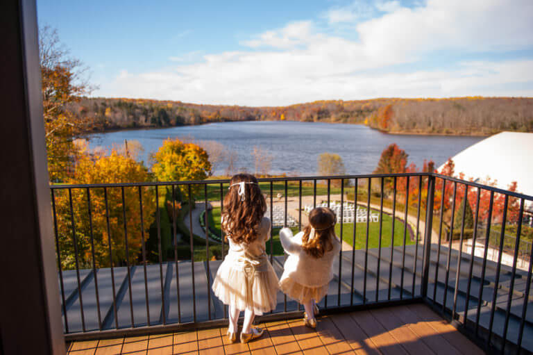 Two girls standing on a balcony overlooking a lake.