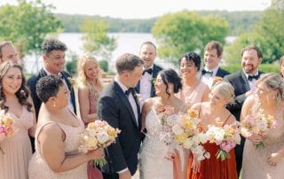 A group of bridesmaids and groomsmen standing in front of a lake during a wedding experience.