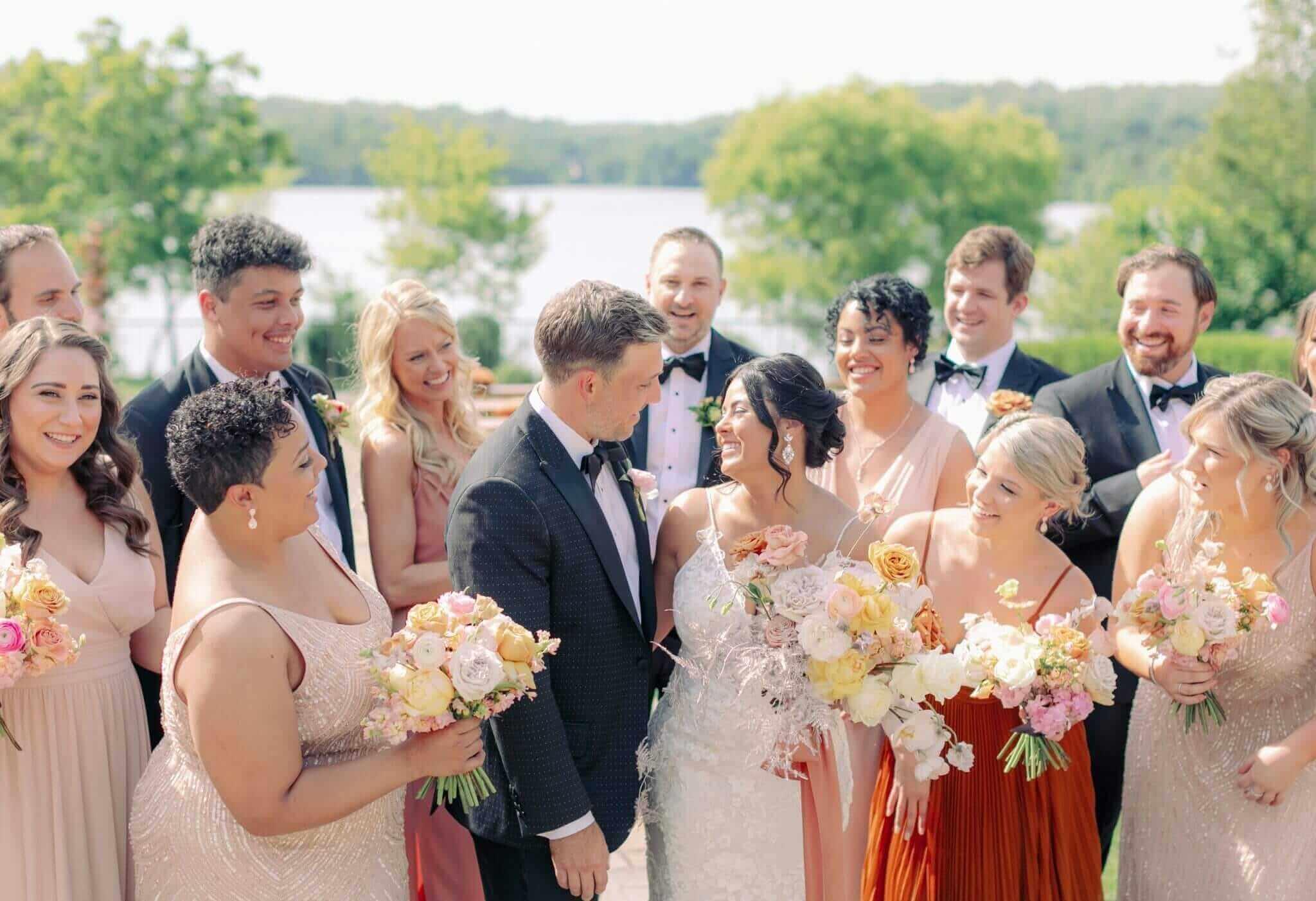 A group of bridesmaids and groomsmen standing in front of a lake during a wedding experience.