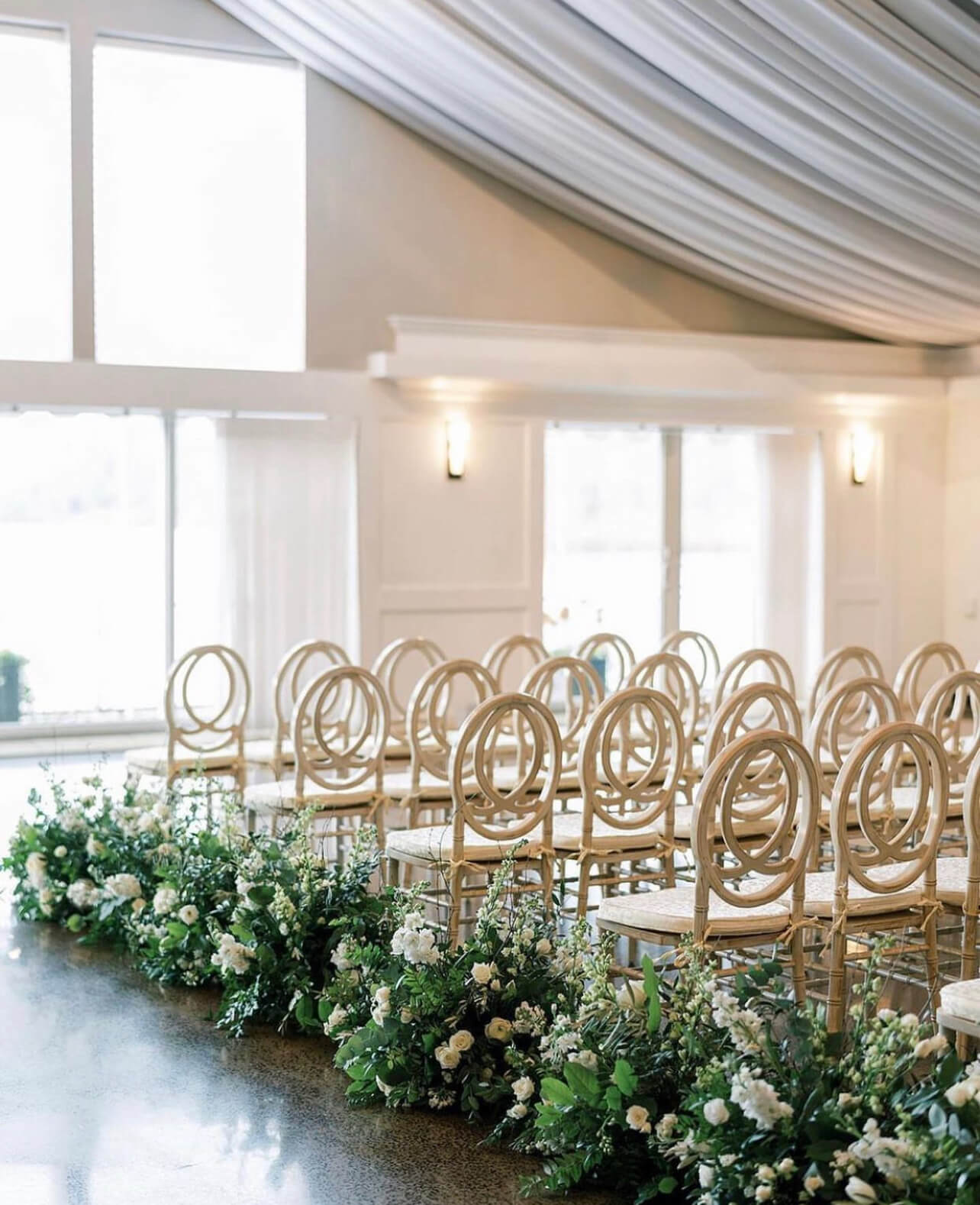 A wedding ceremony set up with white chairs and greenery.