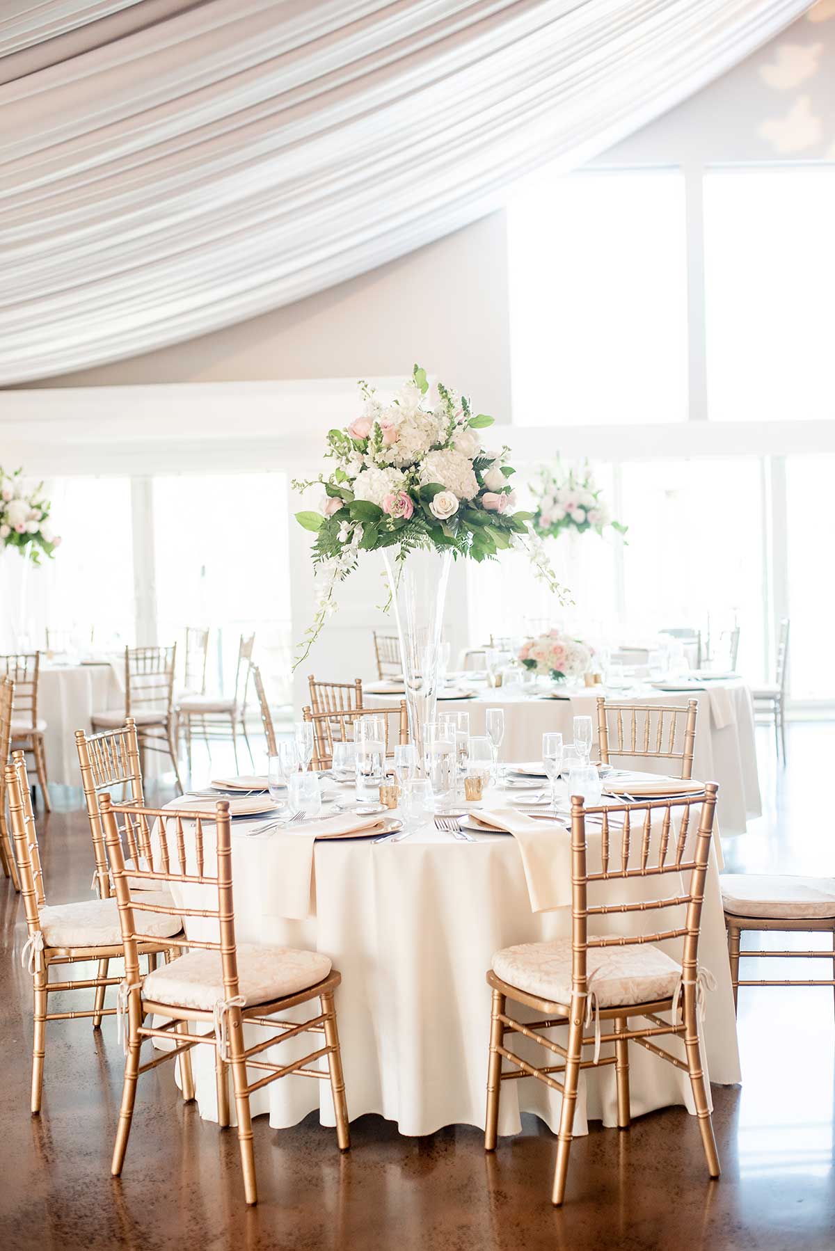 A wedding reception set up with white tables and chairs.