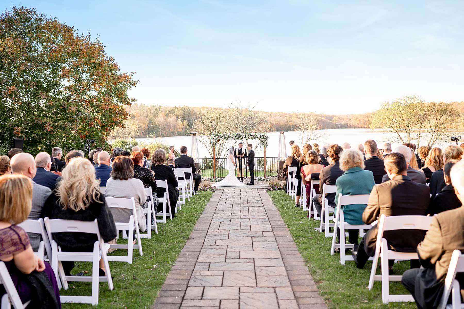 A wedding ceremony at a lake with chairs in the background.
