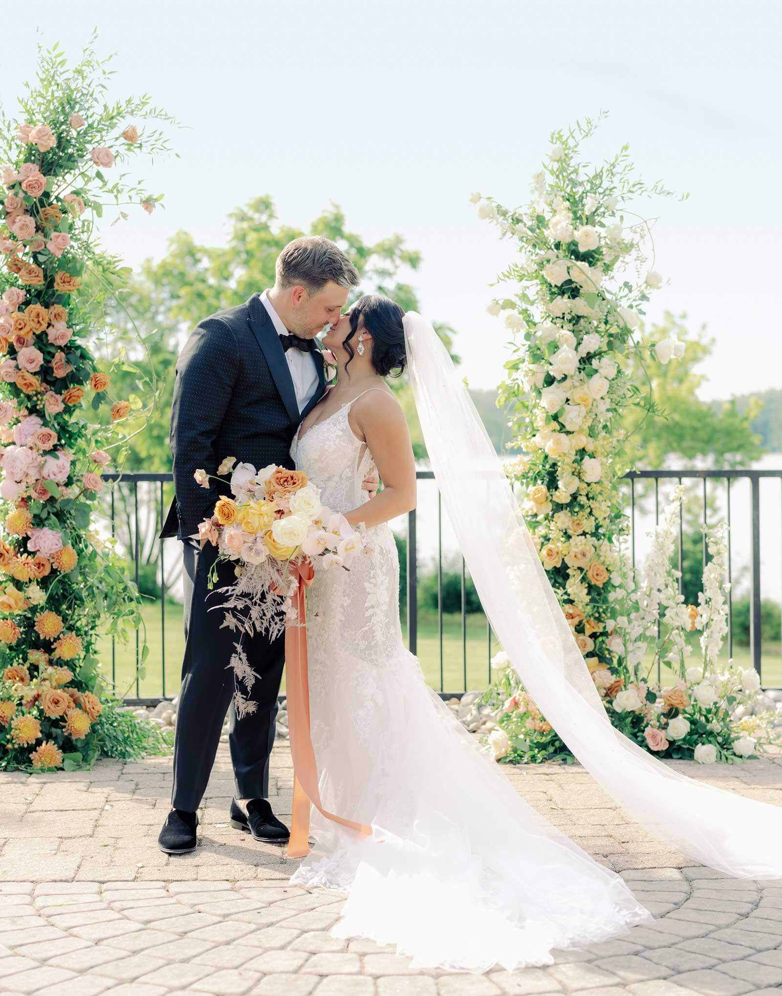 A bride and groom kiss in front of a floral arch.