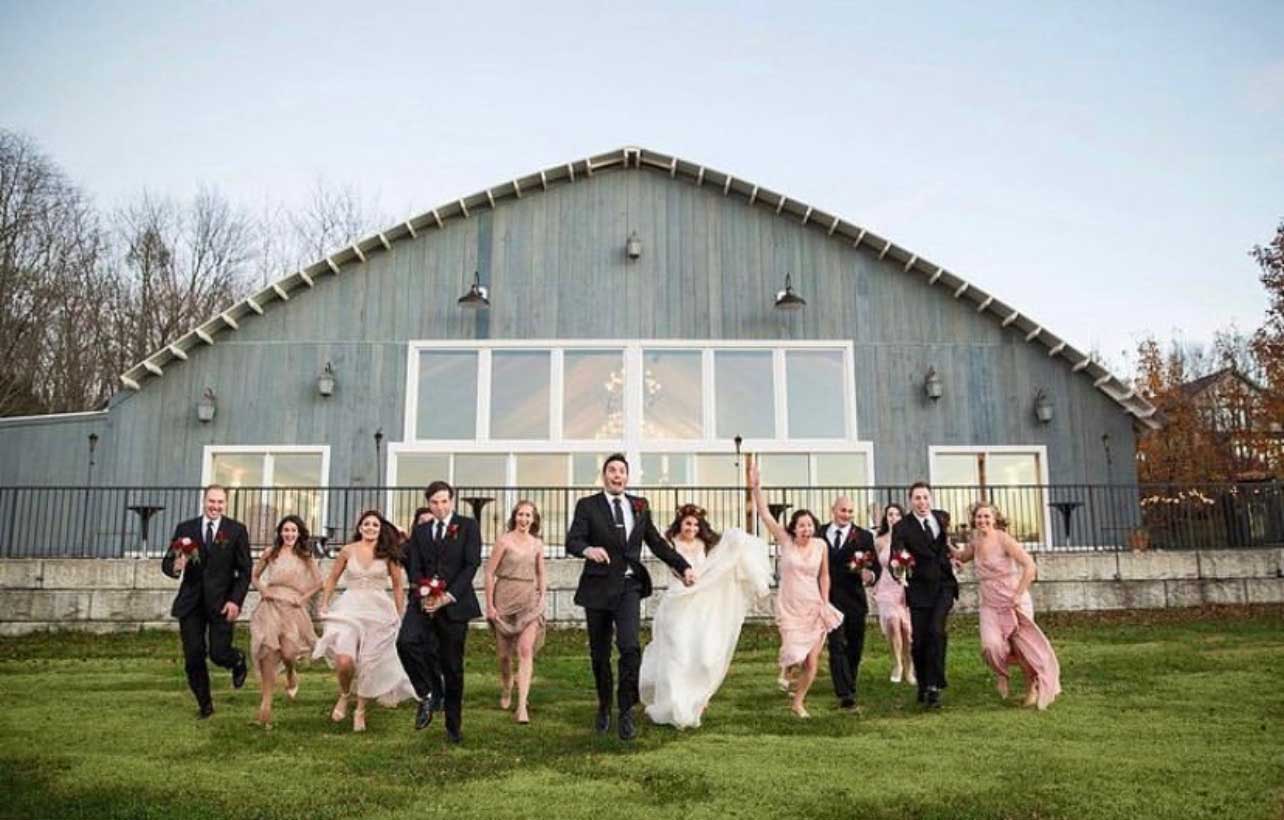 A group of bridesmaids and groomsmen standing in front of a barn.