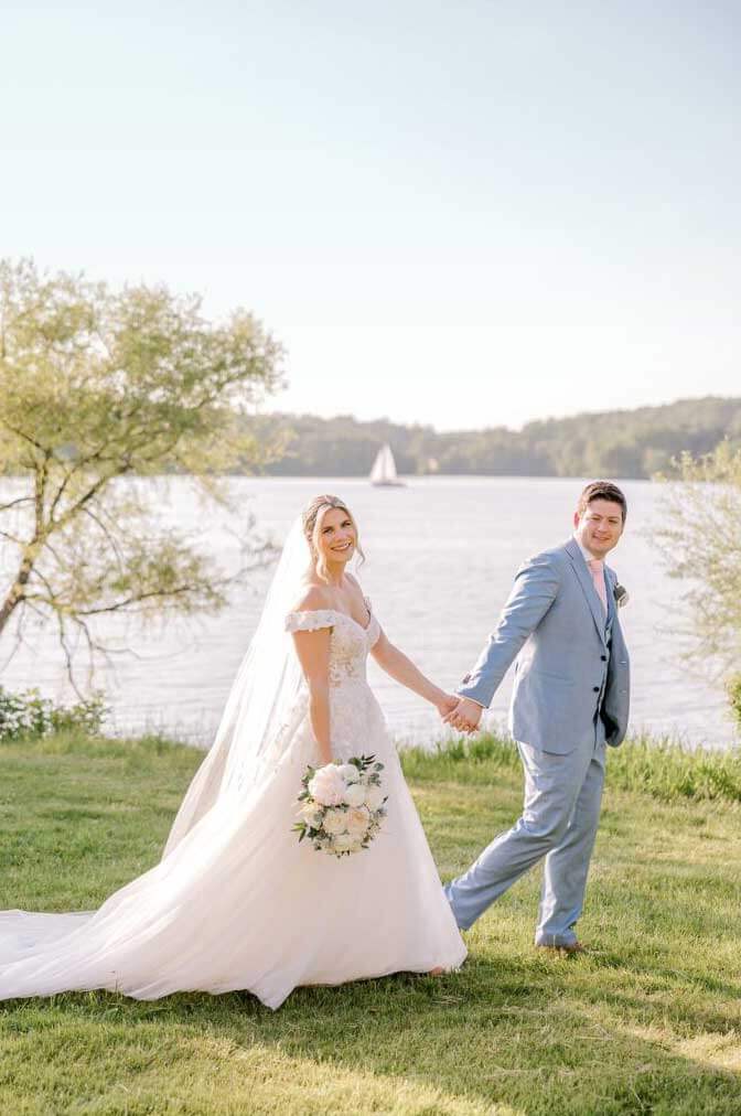 A bride and groom holding hands in front of a lake, celebrating with one of our exclusive wedding packages.