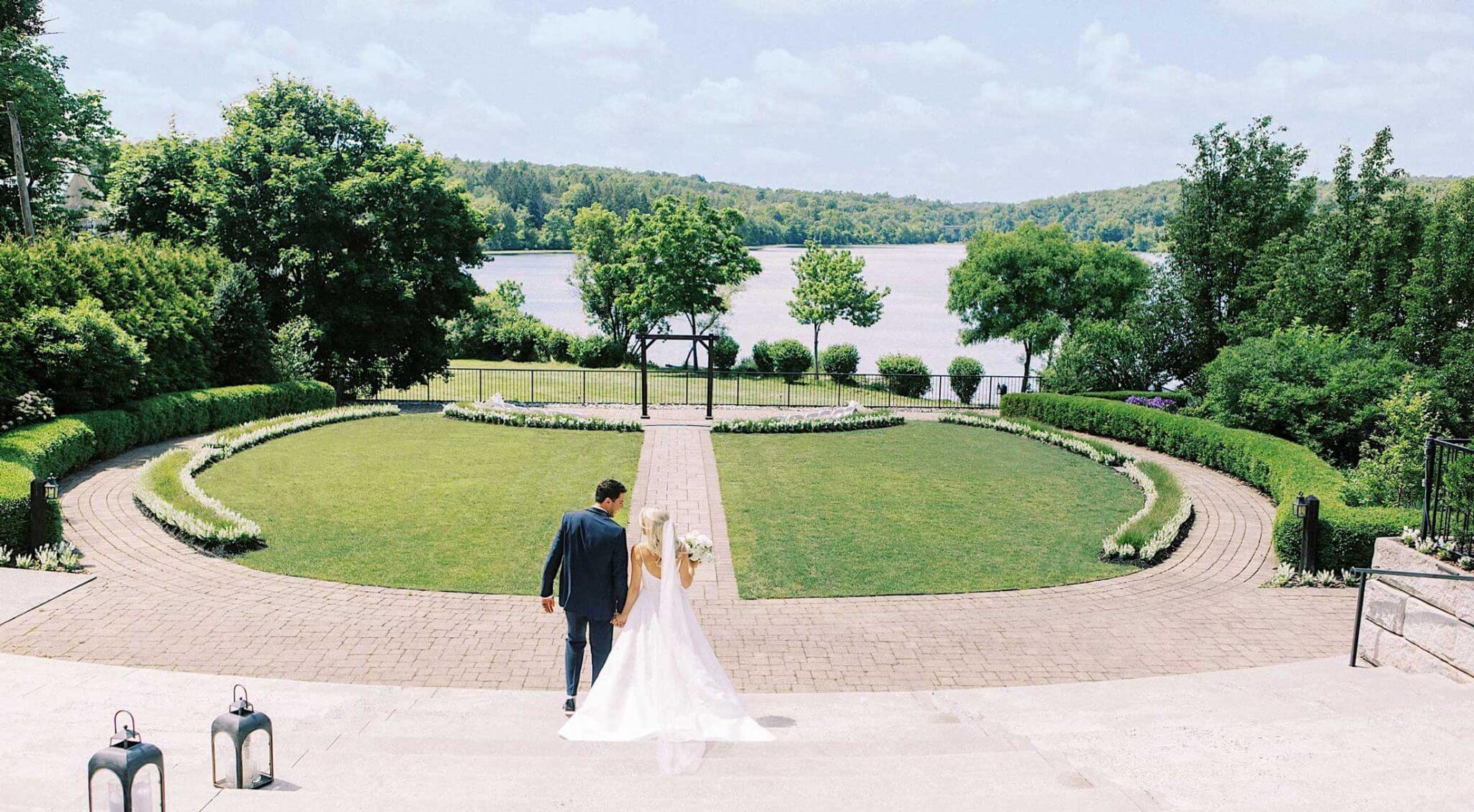 A bride and groom walking down a path in front of a lake.