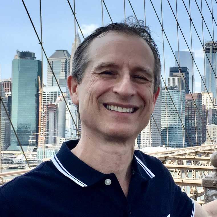 A man smiling in front of the brooklyn bridge.
