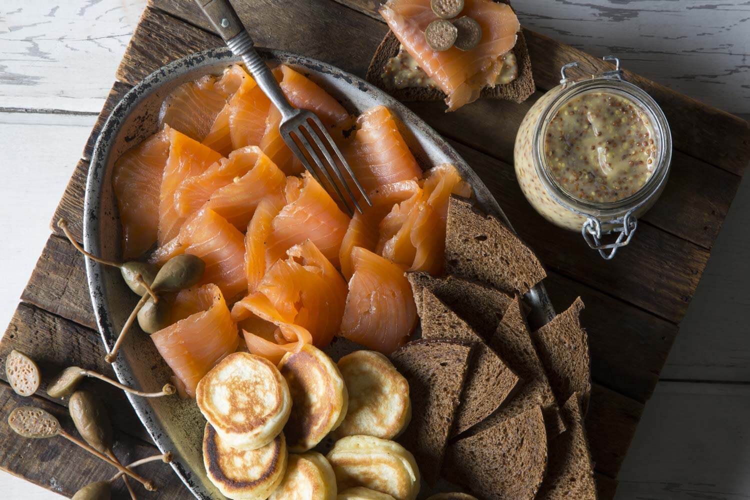 A plate with salmon, crackers and a jar of mustard.
