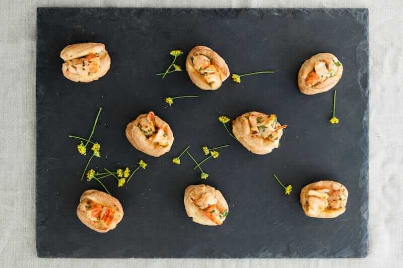 Assorted shrimp canapés elegantly arranged on a slate serving platter with garnishes.