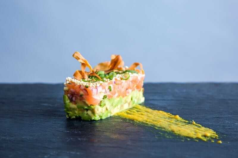 Salmon tartare with avocado on a slate surface with a smear of sauce.